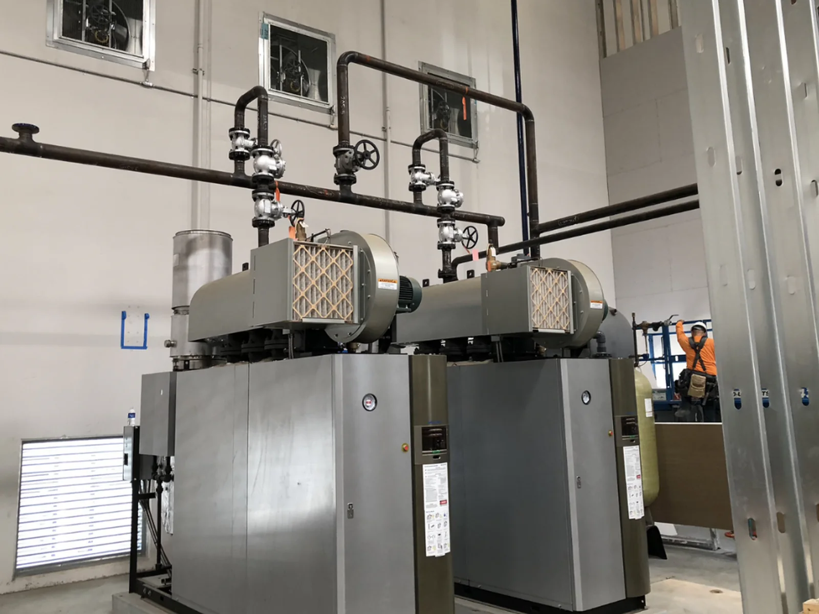 Twin industrial boiler units with piping and controls inside a mechanical room