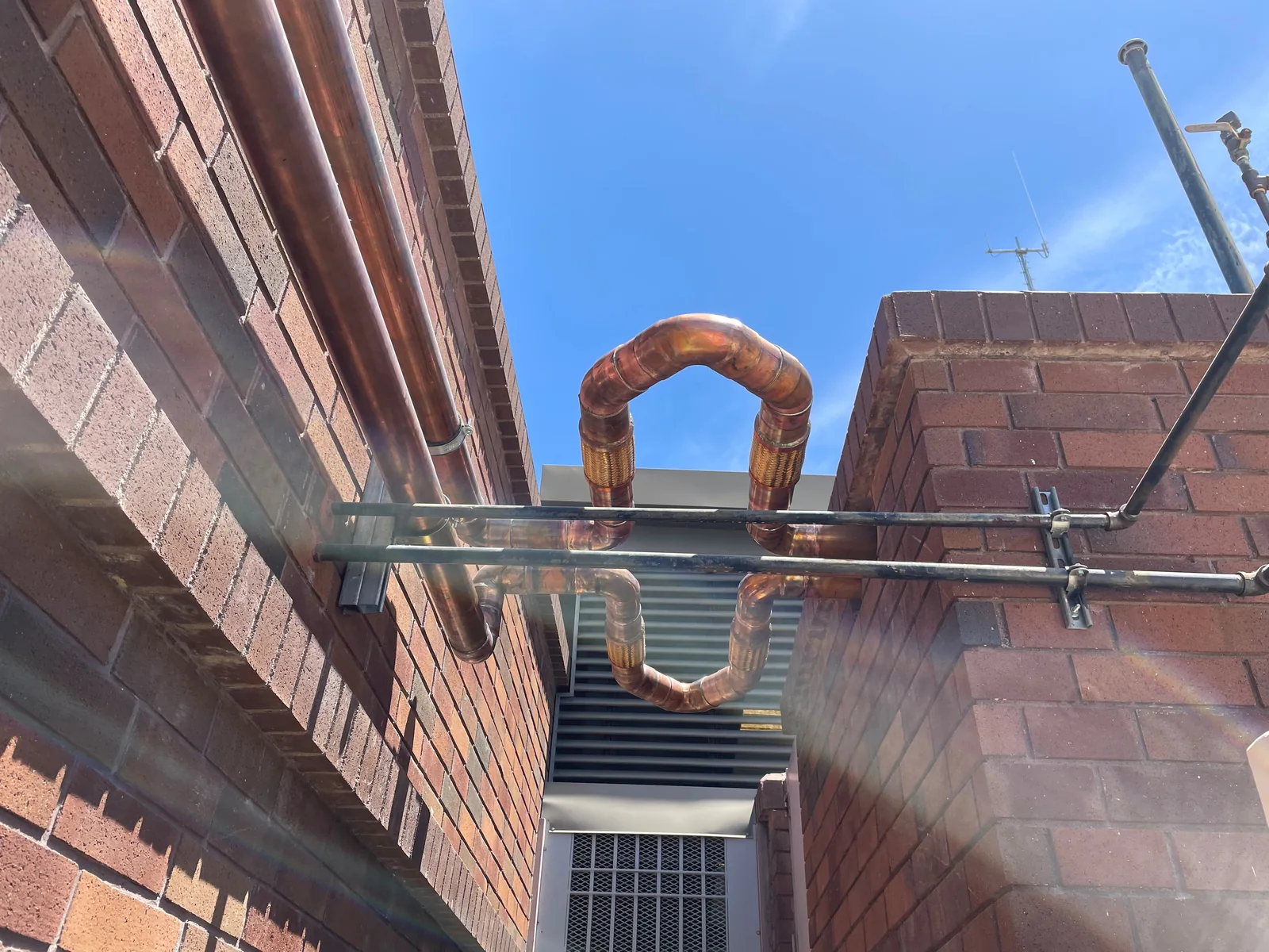 Exterior copper piping and flexible equipment connections between brick walls