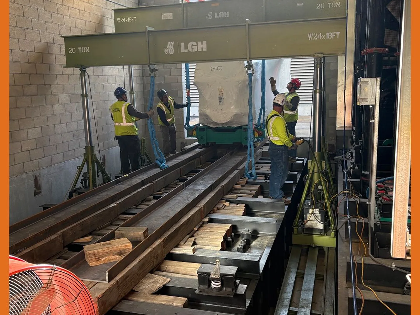 Crew moving wrapped equipment on rails beneath a hydraulic gantry