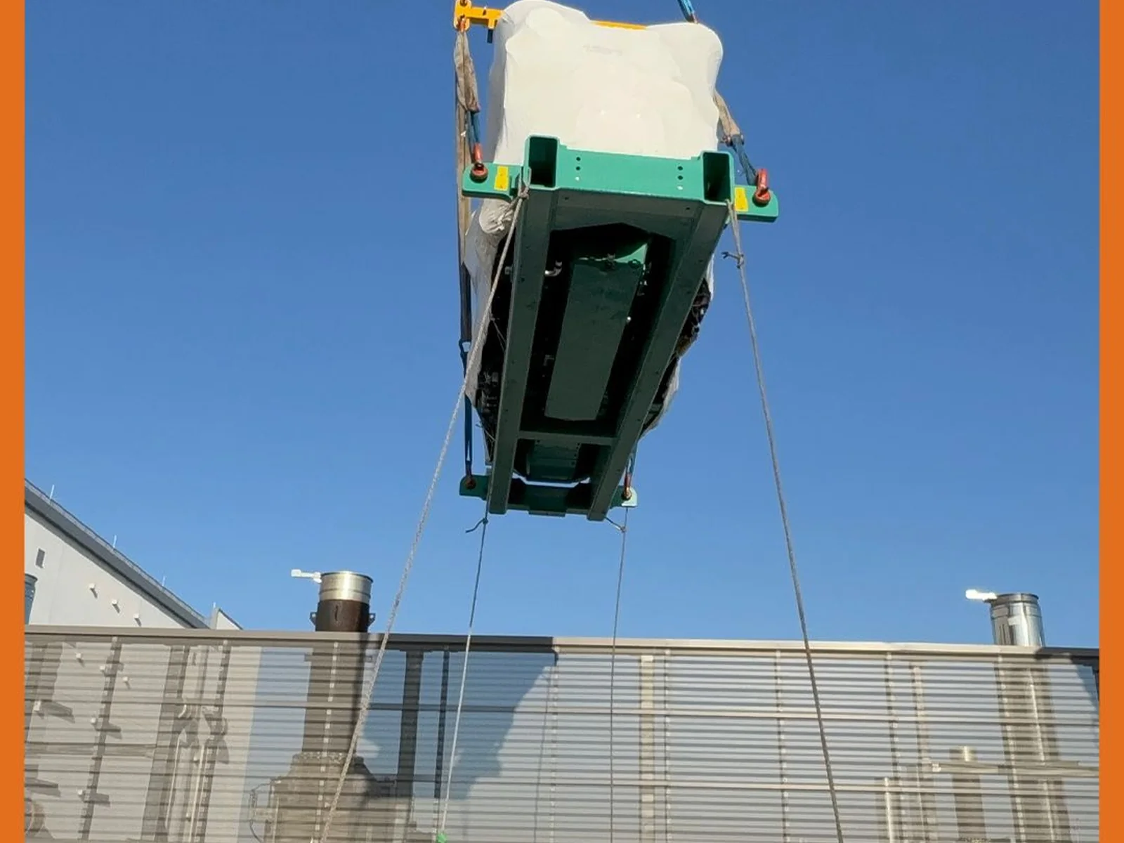 Large wrapped equipment unit being lifted above a rooftop screen wall