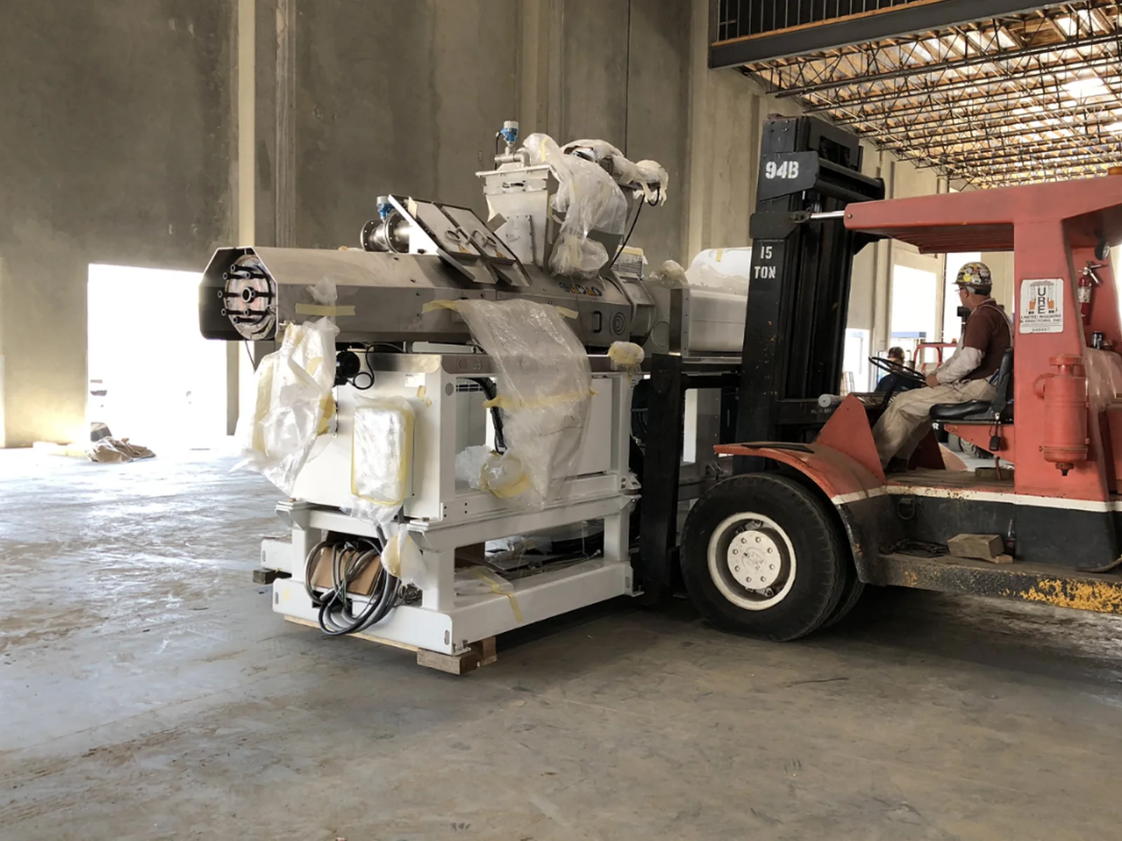 Forklift positioning a large industrial production machine inside a facility