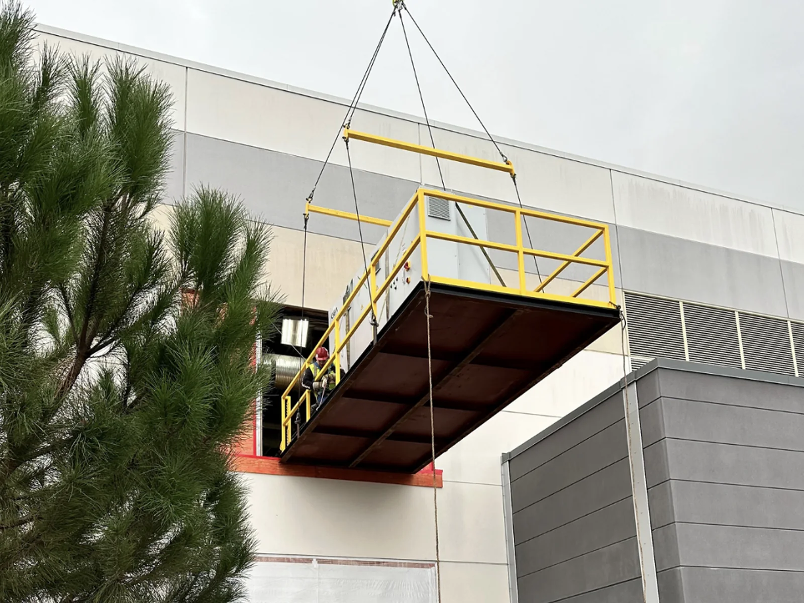 Crane lifting an equipment platform through an exterior facility opening