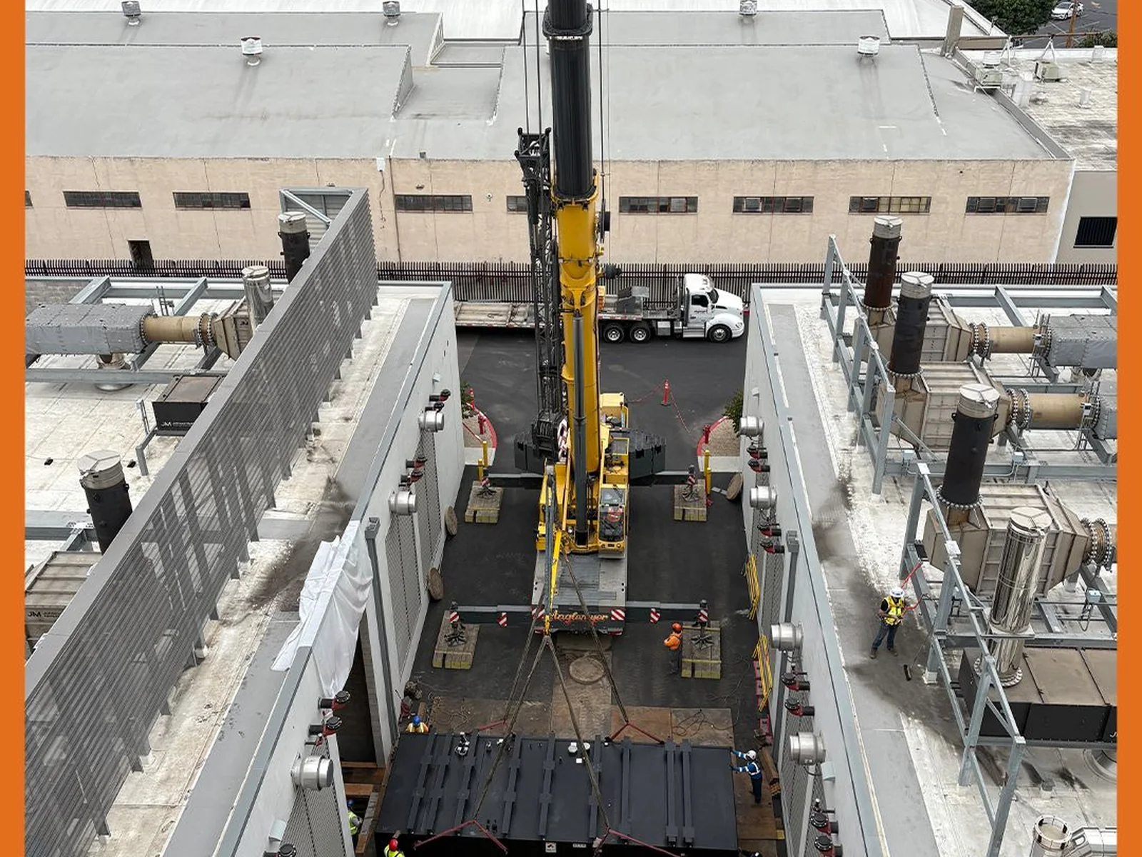 Mobile crane positioned between industrial buildings for rooftop work