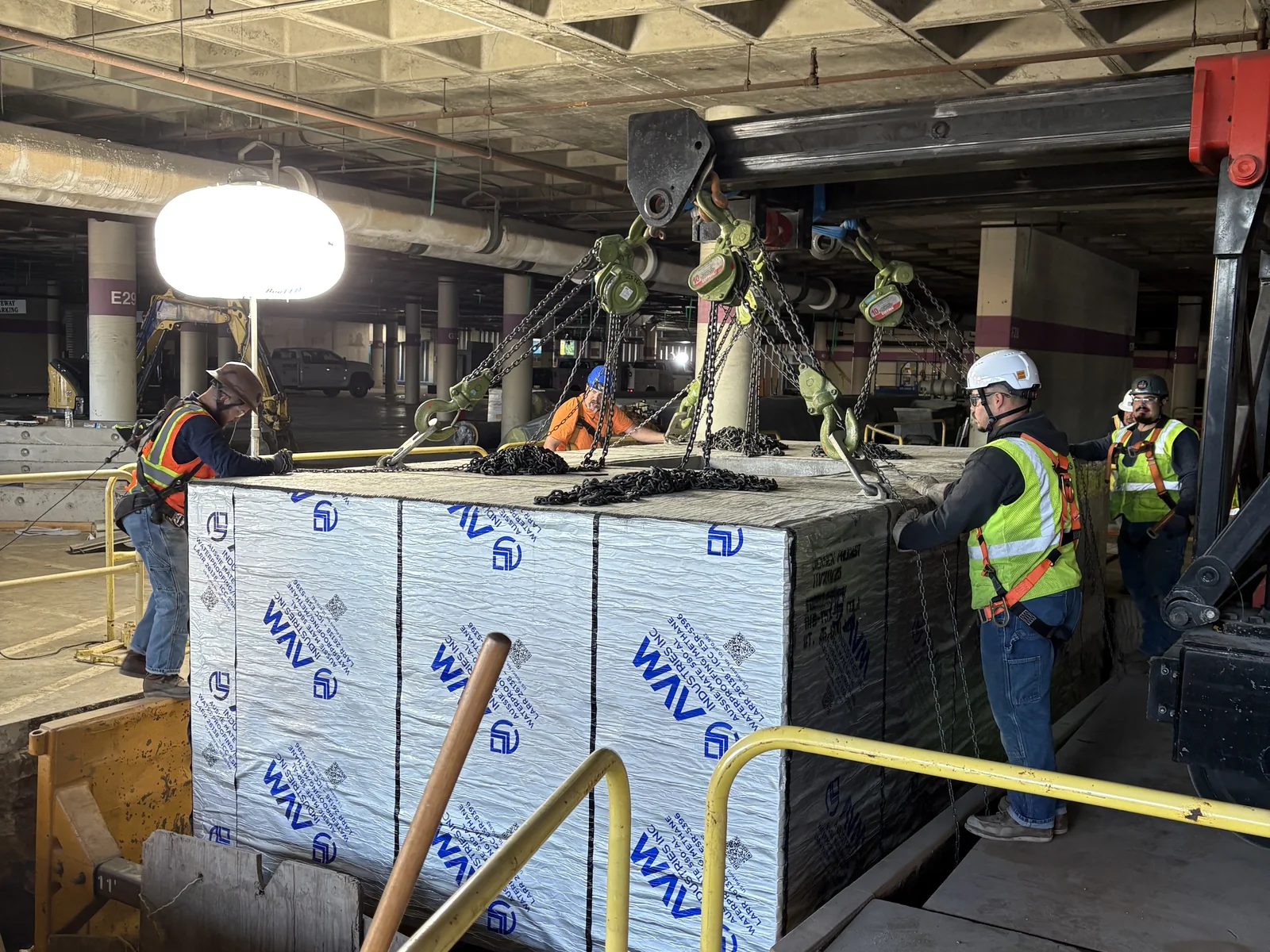 URE crew rigging a large equipment unit with chain hoists in a parking structure
